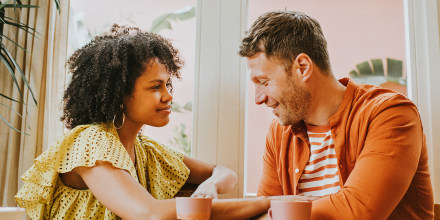 A young couple sit at a dining table sipping hot drinks and flirt.
